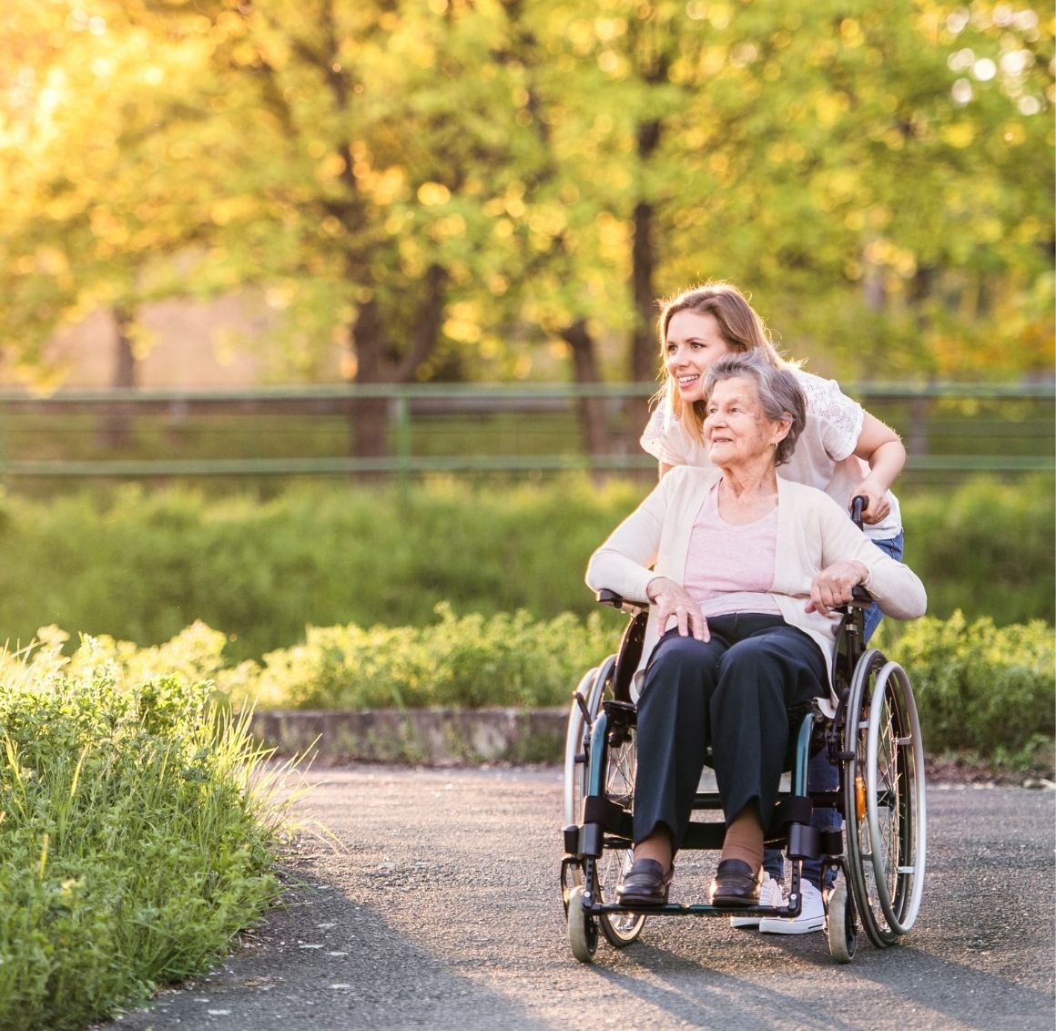 Caregiver Assisting An Elderly Woman In A Wheelchair Outdoors.
