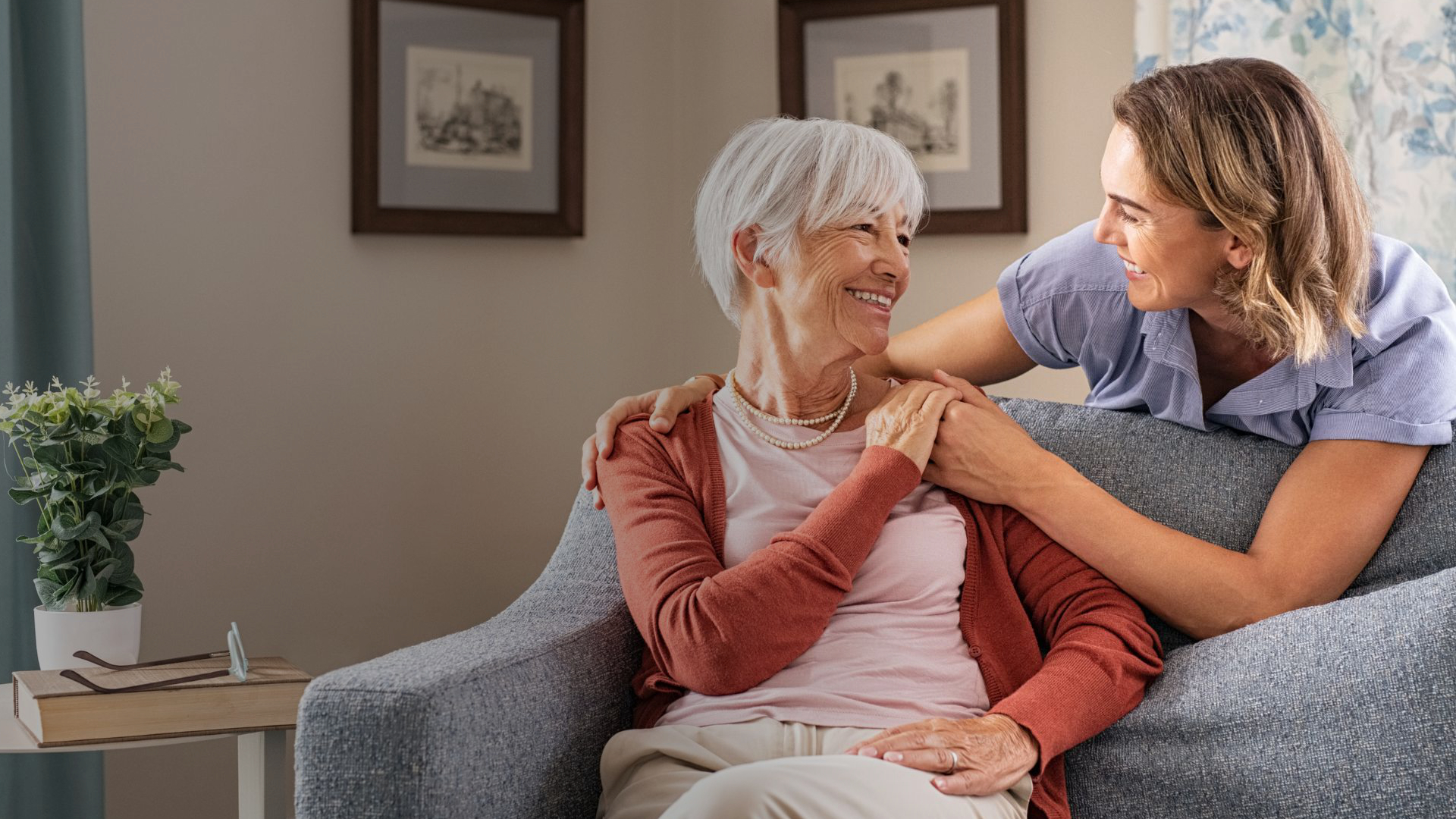 Caregiver offering support to an elderly woman while sitting on a couch.