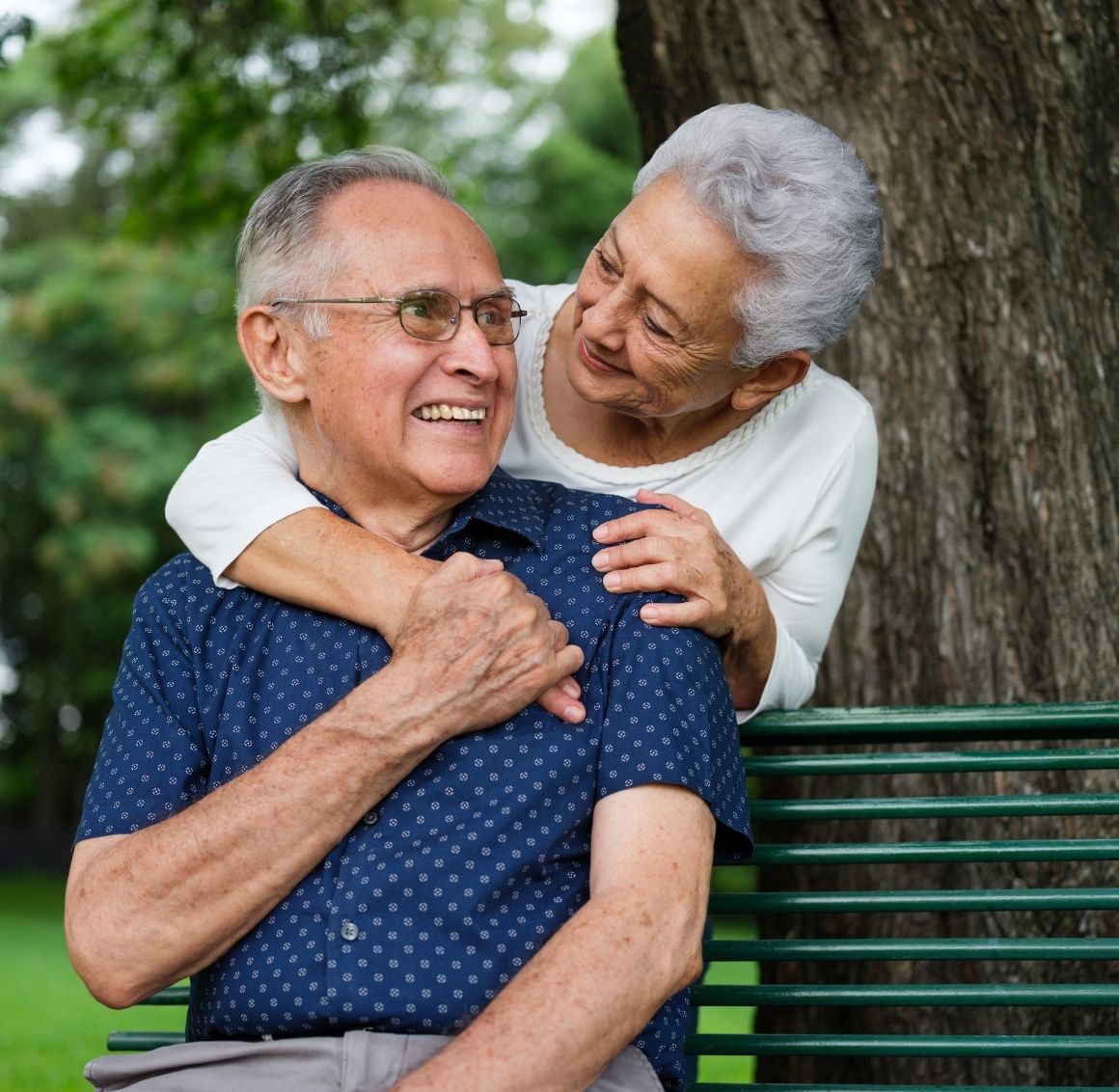 Elderly couple sitting together on a park bench, sharing a warm embrace and emotional support.