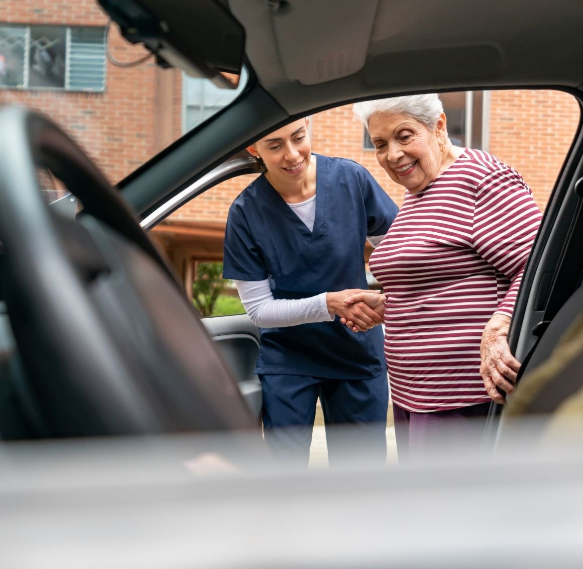 Caregiver helping an elderly woman step into a car, offering support during transportation.