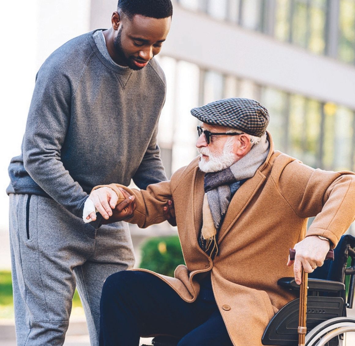 Caregiver helping an elderly man in a wheelchair adjust his position outdoors.
