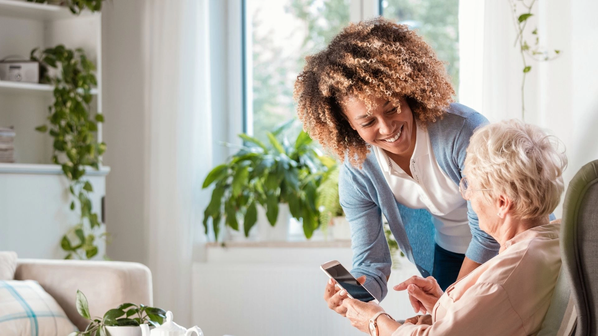 Caregiver assisting a senior woman with reading a digital device