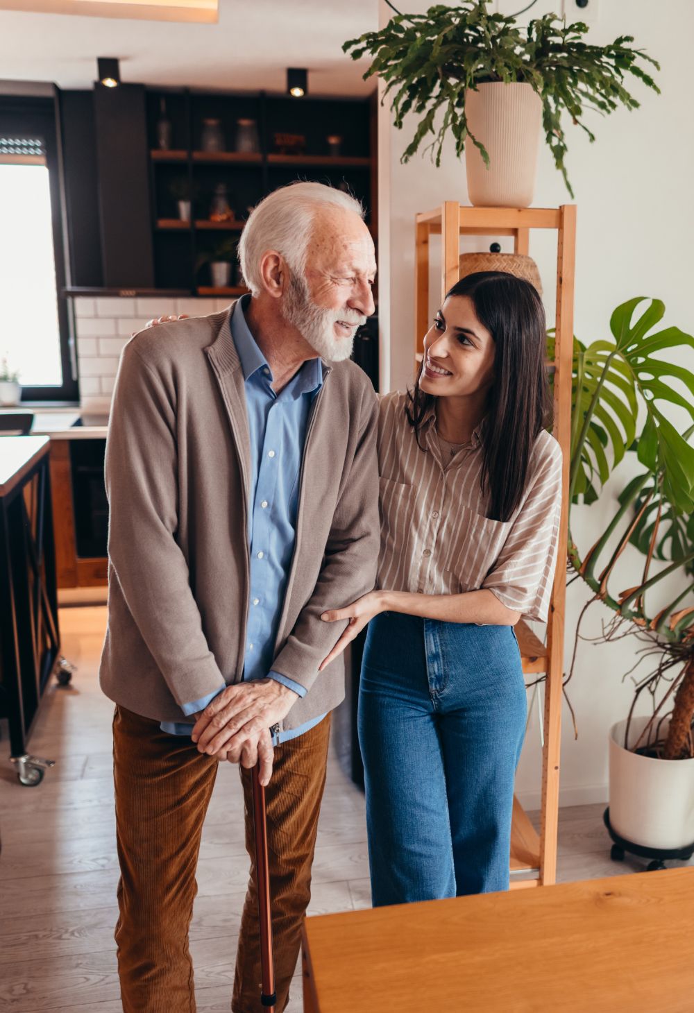 Caregiver supporting an elderly man as he walks with a cane
