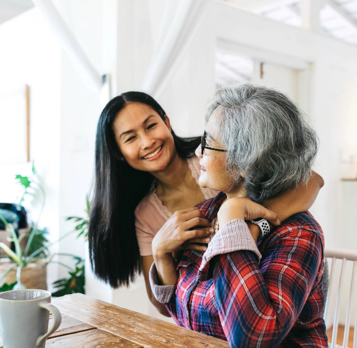 A caregiver offers comforting companionship to an older woman while sitting together at the table.