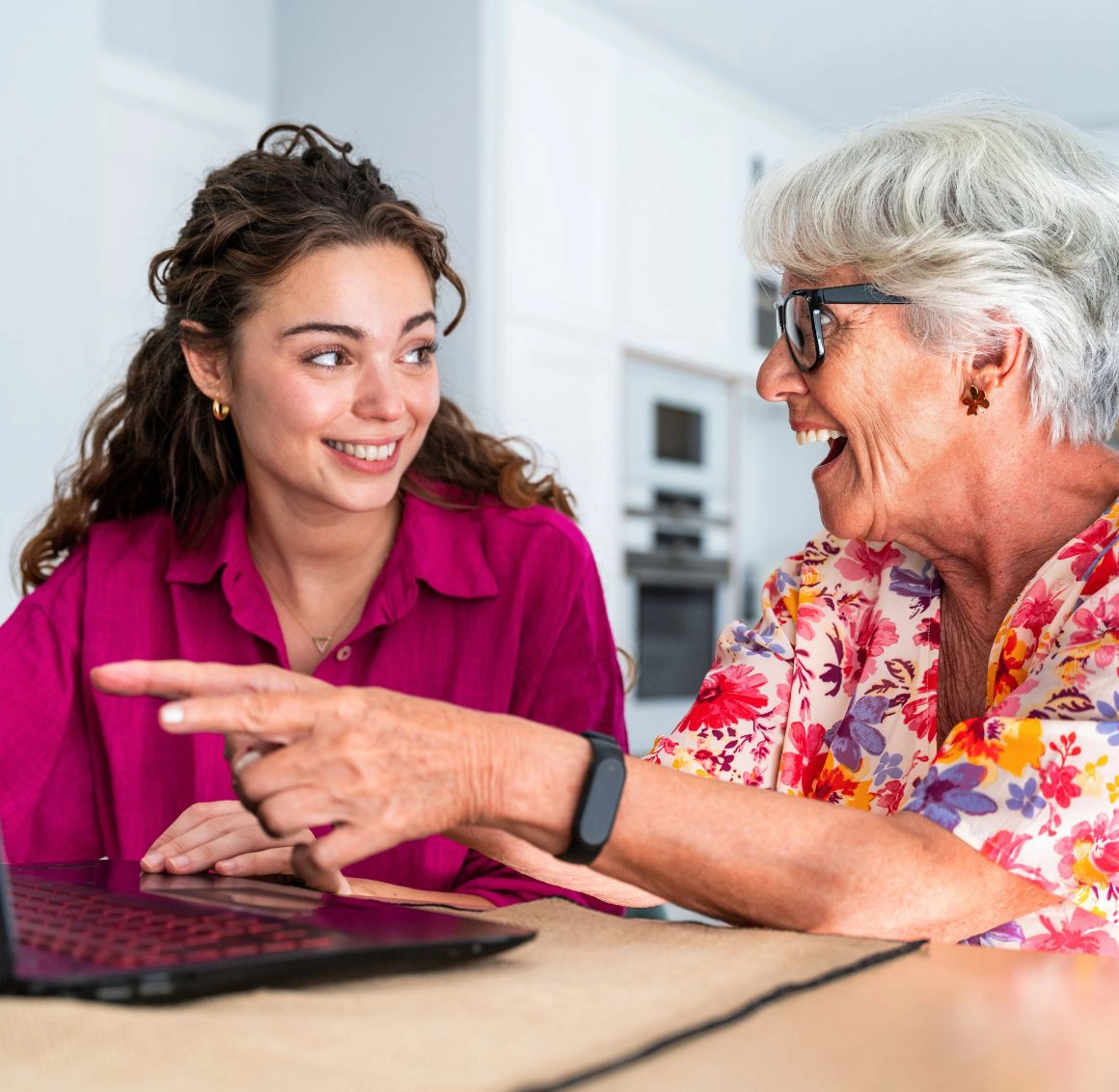 Caregiver helping an older woman use a laptop while smiling together.