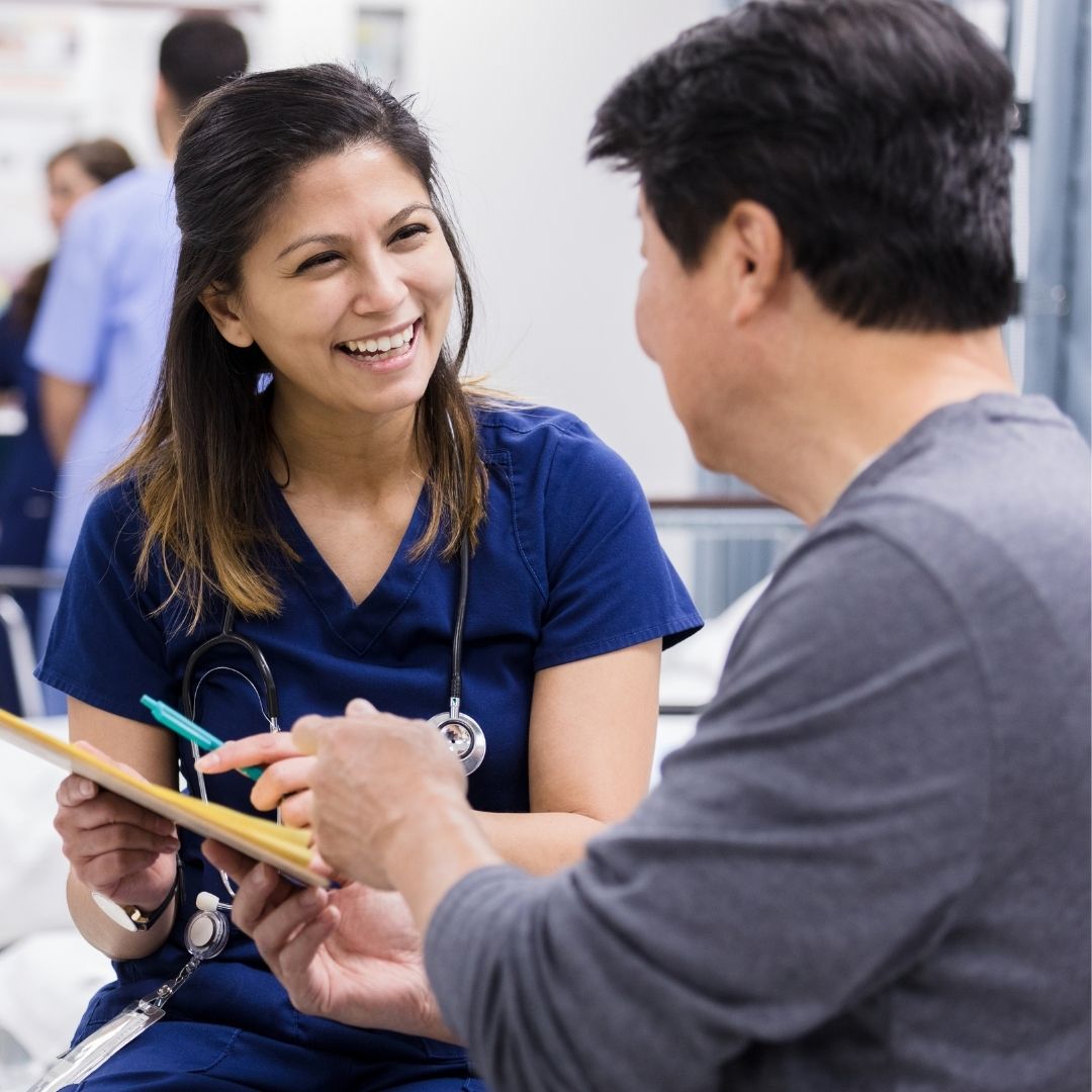 Smiling nurse assisting an older man with paperwork in a clinical setting, highlighting professional home health care support.