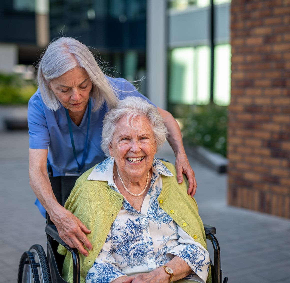 Smiling elderly woman in a wheelchair being assisted by a caregiver outdoors, representing compassionate senior home care in Glendale, CA.