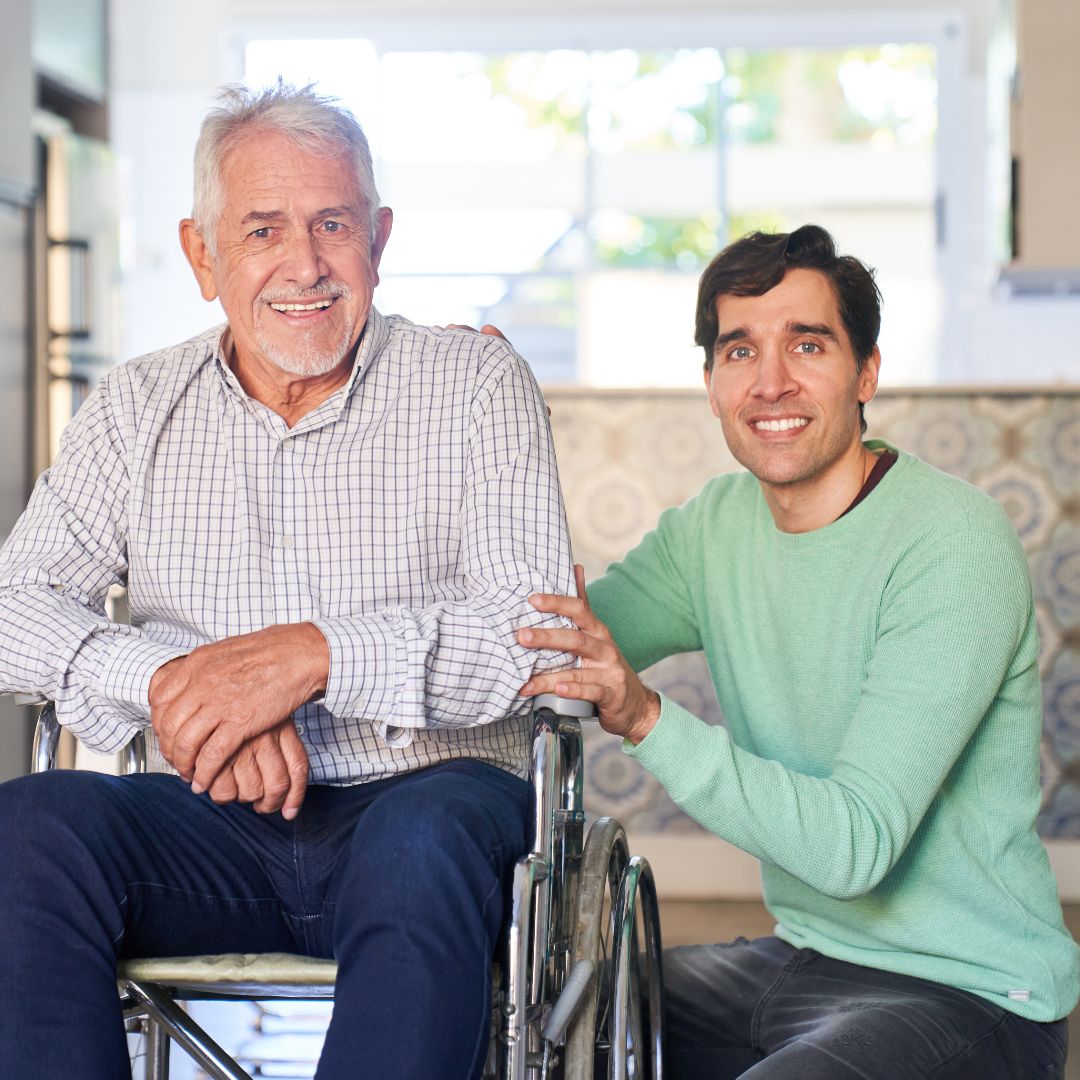 Smiling elderly man in a wheelchair with a supportive family caregiver beside him, representing compassionate home care in Glendale, CA.
